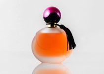 a front view orange designed perfume with black and purple cap isolated on the white floor